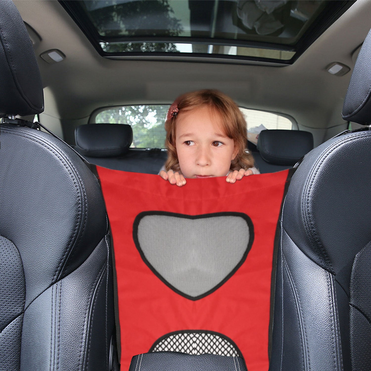 Child peeking from behind a red car seat cover with a heart design in a car.